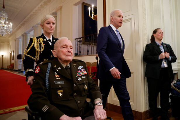 미군 최고등급 훈장인 '명예 훈장'을 받기 위해 랠프 퍼킷 주니어(왼쪽) 대령이 휠체어를 탄 채 백악관 이스트룸에 들어서고 있다. 오른쪽에 조 바이든 미 대통령이 보인다. /로이터 연합뉴스