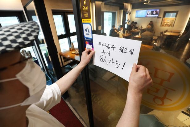 사적모임 제한이 6인에서 8인으로 조정된 18일 서울의 한 식당에서 주인이 8인 가능 안내문을 써 붙이고 있다. /뉴스1
