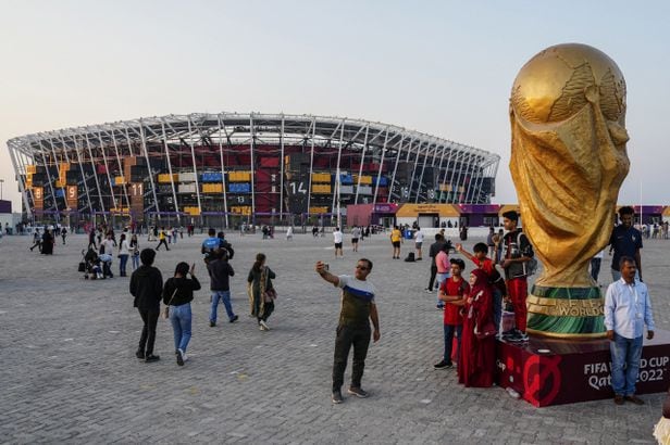 People pose for pictures next to a replica of the World Cup Trophy, right, with the Stadium 974 in the background before the Qatar Fashion United event in Doha, Qatar, Friday, Dec. 16, 2022. (AP Photo