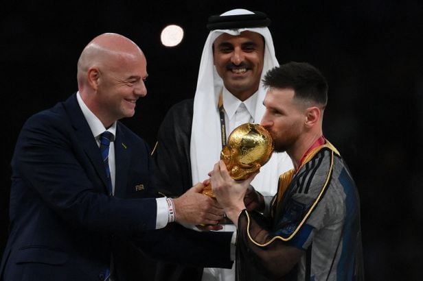 TOPSHOT - Argentina's forward #10 Lionel Messi kisses the World Cup trophy as FIFA President Gianni Infantino and Qatar's Emir Sheikh Tamim bin Hamad al-Thani look on during the Qatar 2022 World Cup trophy ceremony after the football final match between Argentina and France at Lusail Stadium in Lusail, north of Doha on December 18, 2022. - Argentina won in the penalty shoot-out. (Photo by FRANCK FIFE
